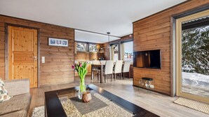 A modern living room with a wooden interior, a dining area, and a TV mounted on the wall.