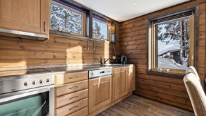 A modern kitchen with wooden cabinetry, a built-in oven, a stove, and a window with a view of a snowy landscape.