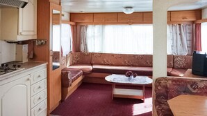 Ein kompaktes Wohnmobil-Interieur mit Küchenzeile, einer Sitzecke mit Sofa und kleinem Tisch sowie einem Fenster mit Vorhängen.