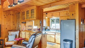 Interior de una cabaña con paredes de madera, una kitchenette, una zona de estar con sofá y sillones, y un cubo de basura.
