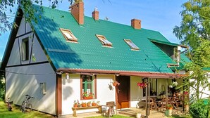 A traditional house with a green roof, a front porch with potted plants, and a bicycle parked outside. - Cozy apartment in Chwarzenko with WiFi (Chwarzenko)