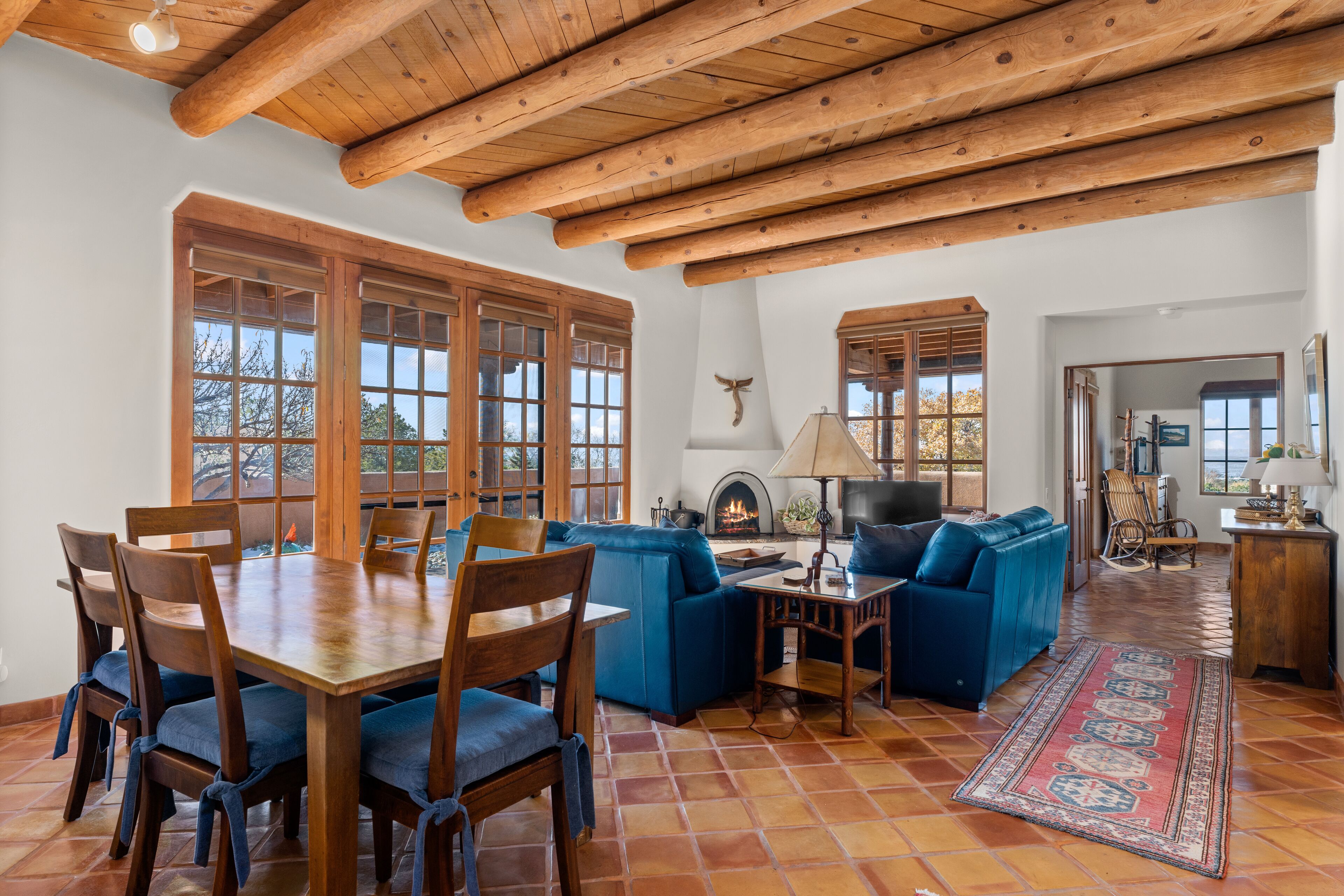 Uma sala ampla com uma mesa de jantar de madeira, sofás azuis e uma lareira.