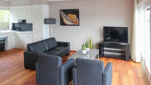 Un saló modern amb un sofà de cuir negre, una taula de centre de vidre i una televisió plana sobre un suport.