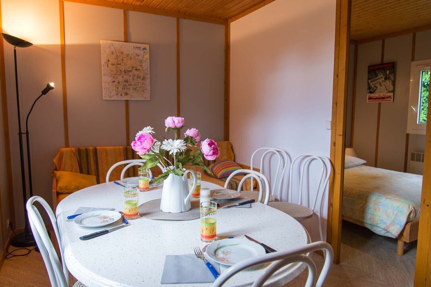A dining area with a round table set for four, white chairs, a vase with flowers, and a map on the wall.