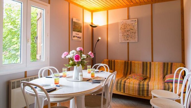 Una habitación acogedora con una mesa redonda, sillas blancas, un sofá con cojín a rayas y un jarrón con flores.