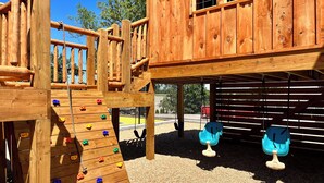 A wooden play structure with climbing walls and swings.