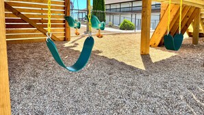 A wooden play structure with swings and a covered area.