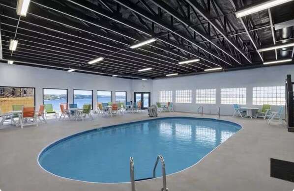An indoor swimming pool with a clear view of the sky through large windows, surrounded by lounge chairs and tables.