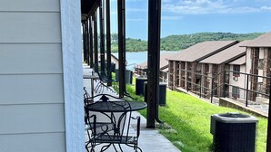 A covered patio area with outdoor seating, a view of a lake, and a building with a brick facade in the background.
