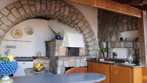 An outdoor kitchen with stone walls, a built-in oven, and a rustic wooden ceiling.