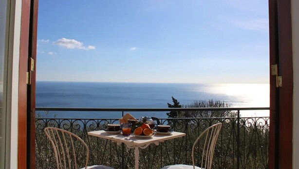 A balcony with a table set for breakfast overlooking a scenic view of the sea.