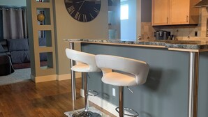 A modern kitchen with a bar area, wooden flooring, and a large wall clock. - Modern, king beds, pools, parks, pet OK, 5 mins toYMCA ,Store and top golf (Meridian)