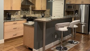 A modern kitchen with wooden cabinets, stainless steel appliances, and a central island with bar stools. - Modern, king beds, pools, parks, pet OK, 5 mins toYMCA ,Store and top golf (Meridian)
