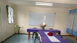 Une salle de conférence avec une longue table recouverte d’une nappe violette, un tableau blanc et un sol carrelé.