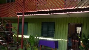 Un bâtiment à l’extérieur vert, avec un escalier en bois et une table recouverte d’une nappe violette.