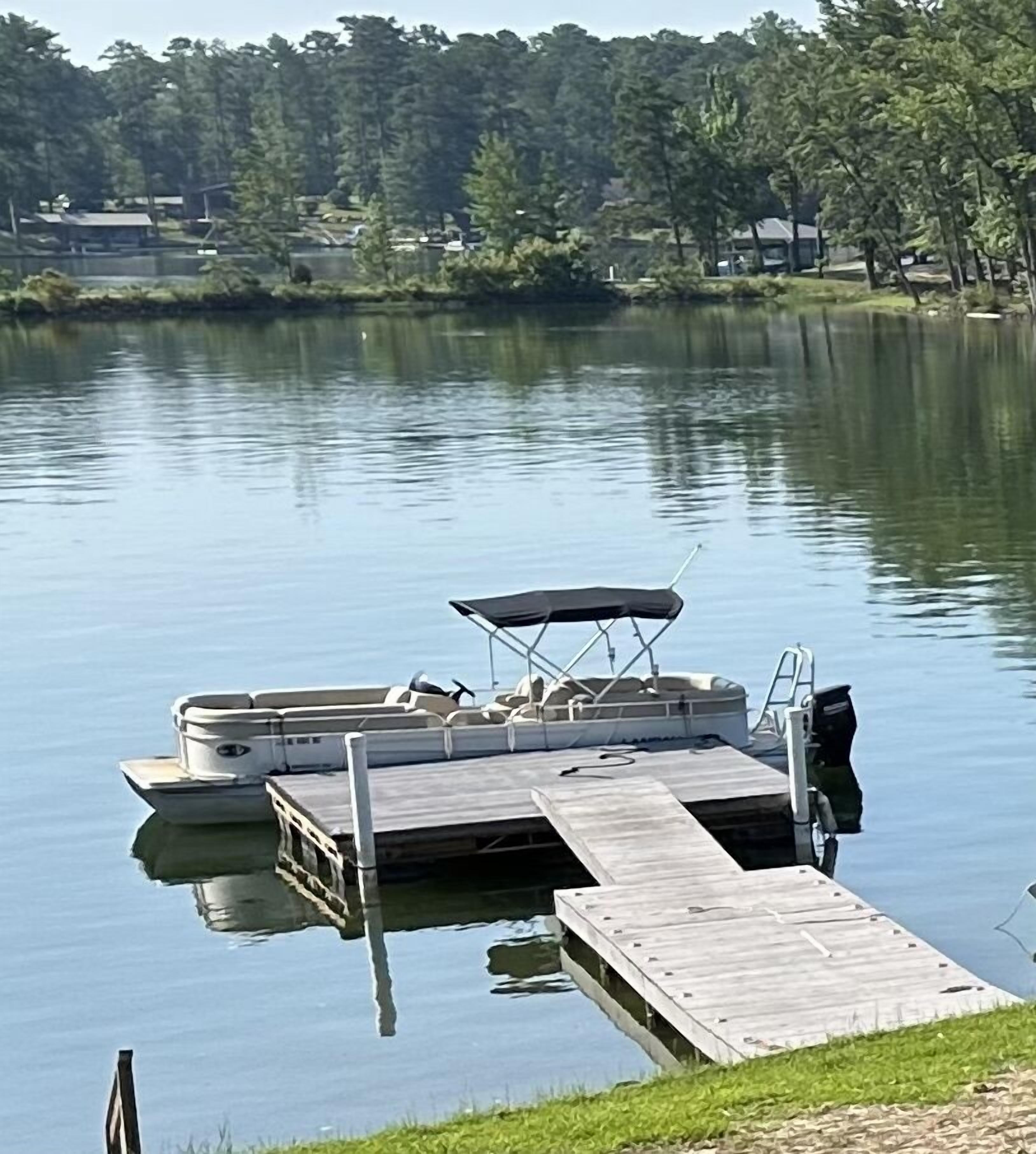 A docked pontoon boat with a canopy and a motor at the end of a wooden pier.