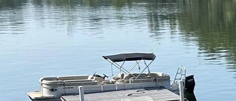 A docked pontoon boat with a canopy and a motor at the end of a wooden pier.