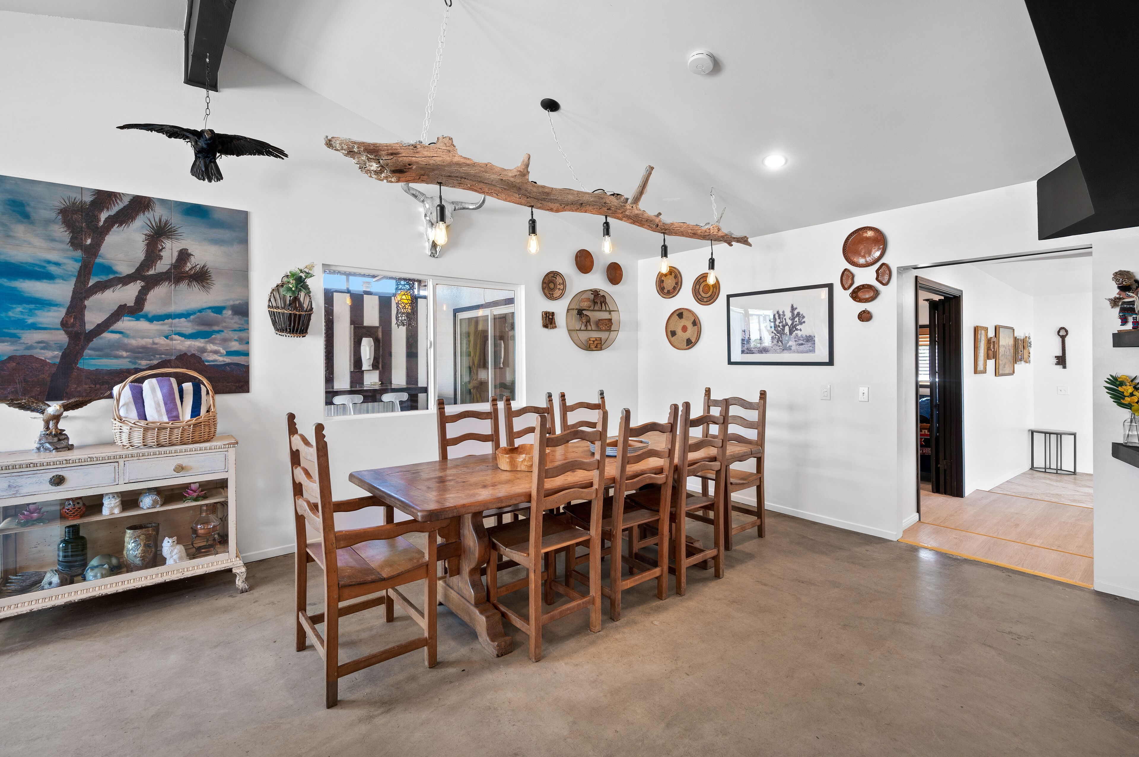 A dining area with a wooden table and chairs, a hanging light fixture, and wall decorations.