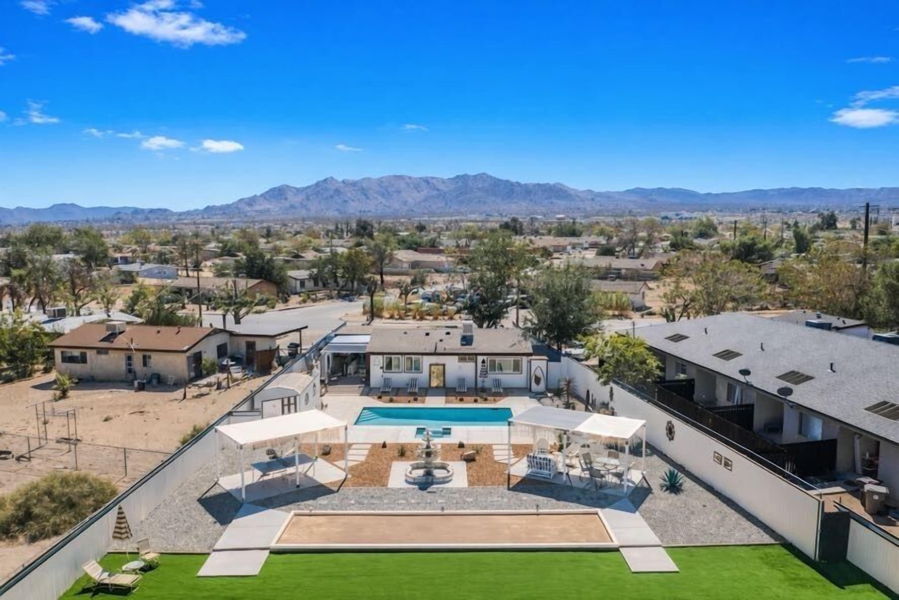 A residential area with a large swimming pool, a tennis court, and a mountain range in the background.