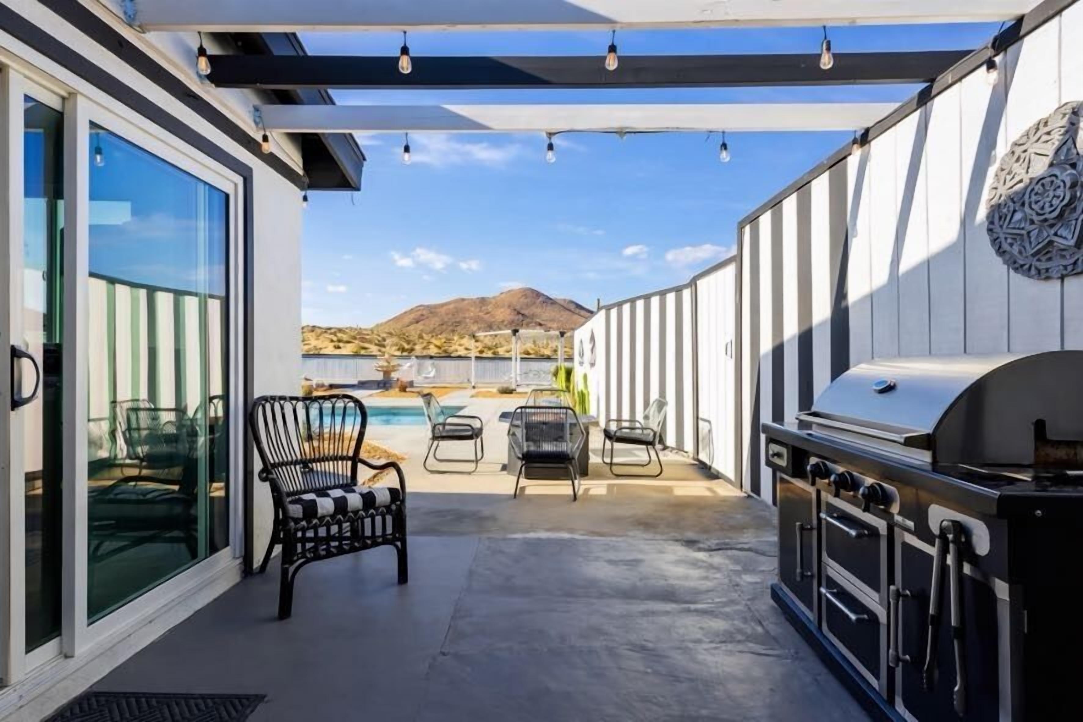 An outdoor patio with a grill, seating area, and a pool view.