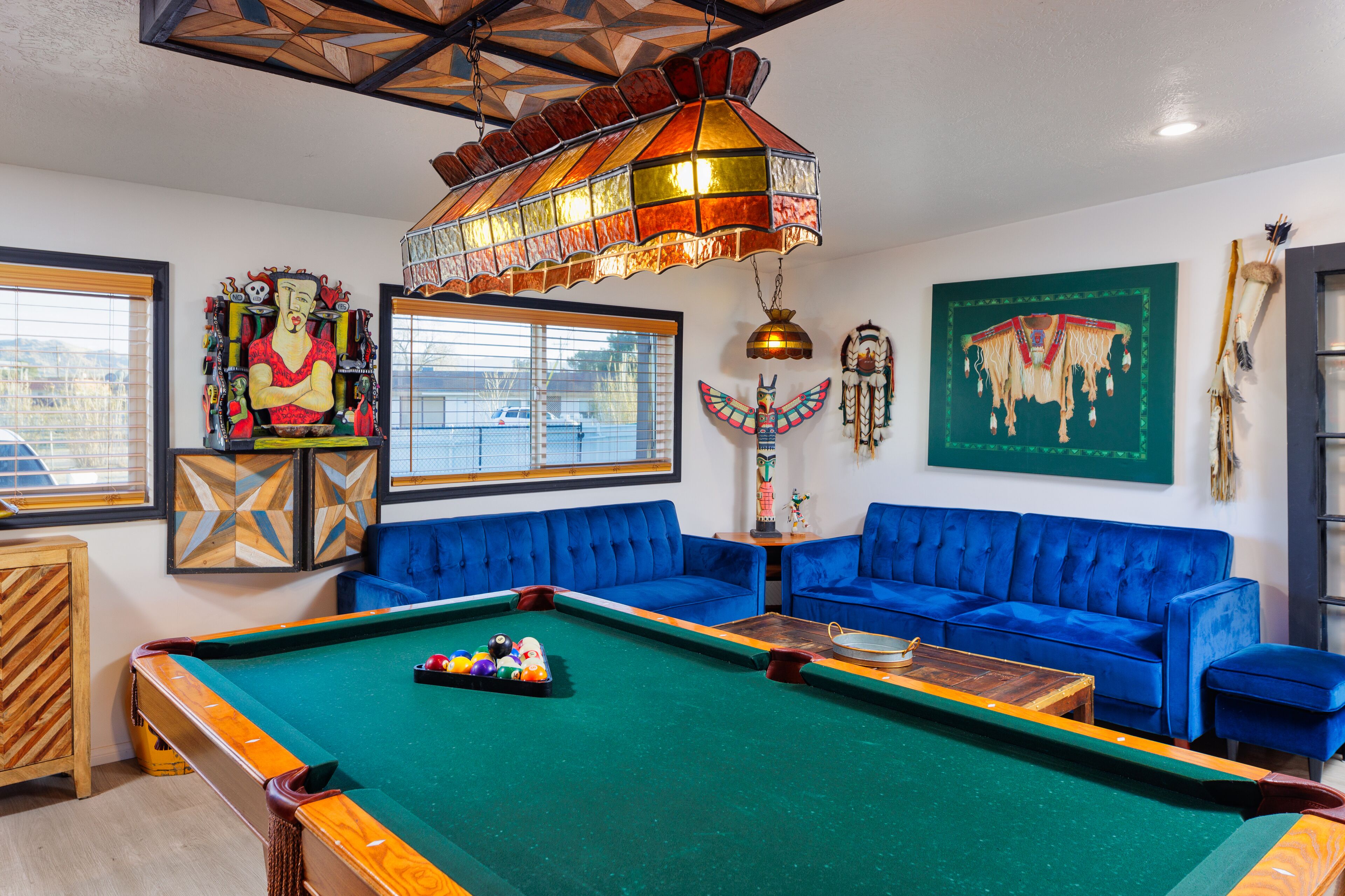 A pool table with a colorful chandelier, a blue sofa, and various wall decorations.