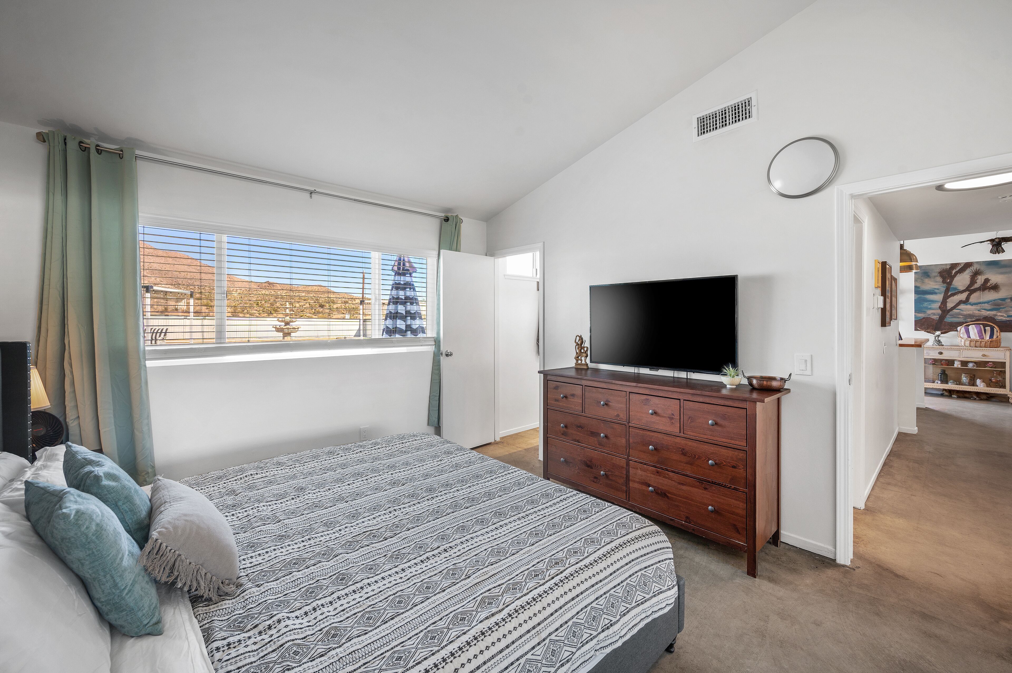 Une chambre à coucher comprenant un lit, une télévision, une commode et une fenêtre donnant sur l’extérieur.