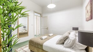 Une chambre à coucher avec un lit, une lampe de chevet, un miroir, une porte et une plante en pot.