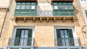 Une façade d’immeuble avec deux fenêtres, chacune dotée de volets verts et d’un balcon avec une rambarde en métal.
