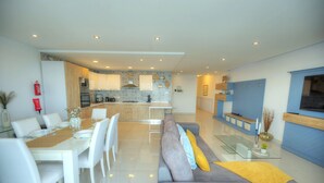 A modern kitchen with white cabinets, a central island, and a dining area with a white table and chairs. - Modern, large 3bedroom, spectacular views GOSLM-9 (Sliema)