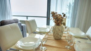 A dining table set with plates, glasses, and cutlery, a vase with dried flowers, and a view of the sea through large windows. - Modern, large 3bedroom, spectacular views GOSLM-9 (Sliema)
