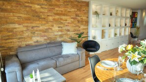 Una sala de estar moderna con un sofá gris, una mesa de comedor de madera dispuesta para dos personas y una pared de ladrillo.