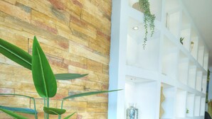 Una habitación con suelo de madera, una planta en maceta, una silla moderna y un estante blanco con plantas.
