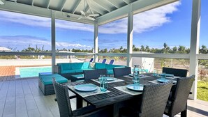 A covered outdoor dining area with a pool in the background.