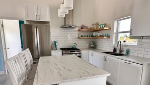 A modern kitchen with white cabinetry, a marble countertop, a built-in oven, and a stainless steel refrigerator.