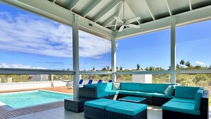 A covered outdoor area with a pool, a large sectional sofa, and lounge chairs.