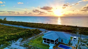A house with a large glass window, a swimming pool, and a view of the ocean at sunset.