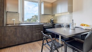 A modern kitchen with dark cabinetry, a gas stove, a coffee maker, and a dining area with a table and chairs. - 1 bedroom lovely apartment in Recco (Recco)