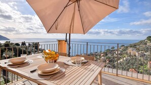 A table set with plates, cutlery, and a fruit basket under a large umbrella, overlooking a coastal view. - 1 bedroom lovely apartment in Recco (Recco)