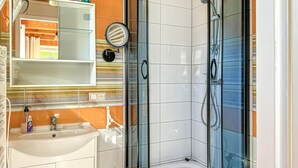 Et moderne badeværelse med en glasbrusekabine, en hvid vask og et spejl over vasken.