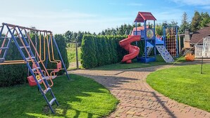 En legeplads med en rød rutchebane, klatrestrukturer og et blåt legehus.