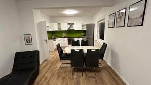 Une cuisine moderne avec des meubles blancs, un pare-feu vert et un coin repas comprenant une table blanche et des chaises noires.