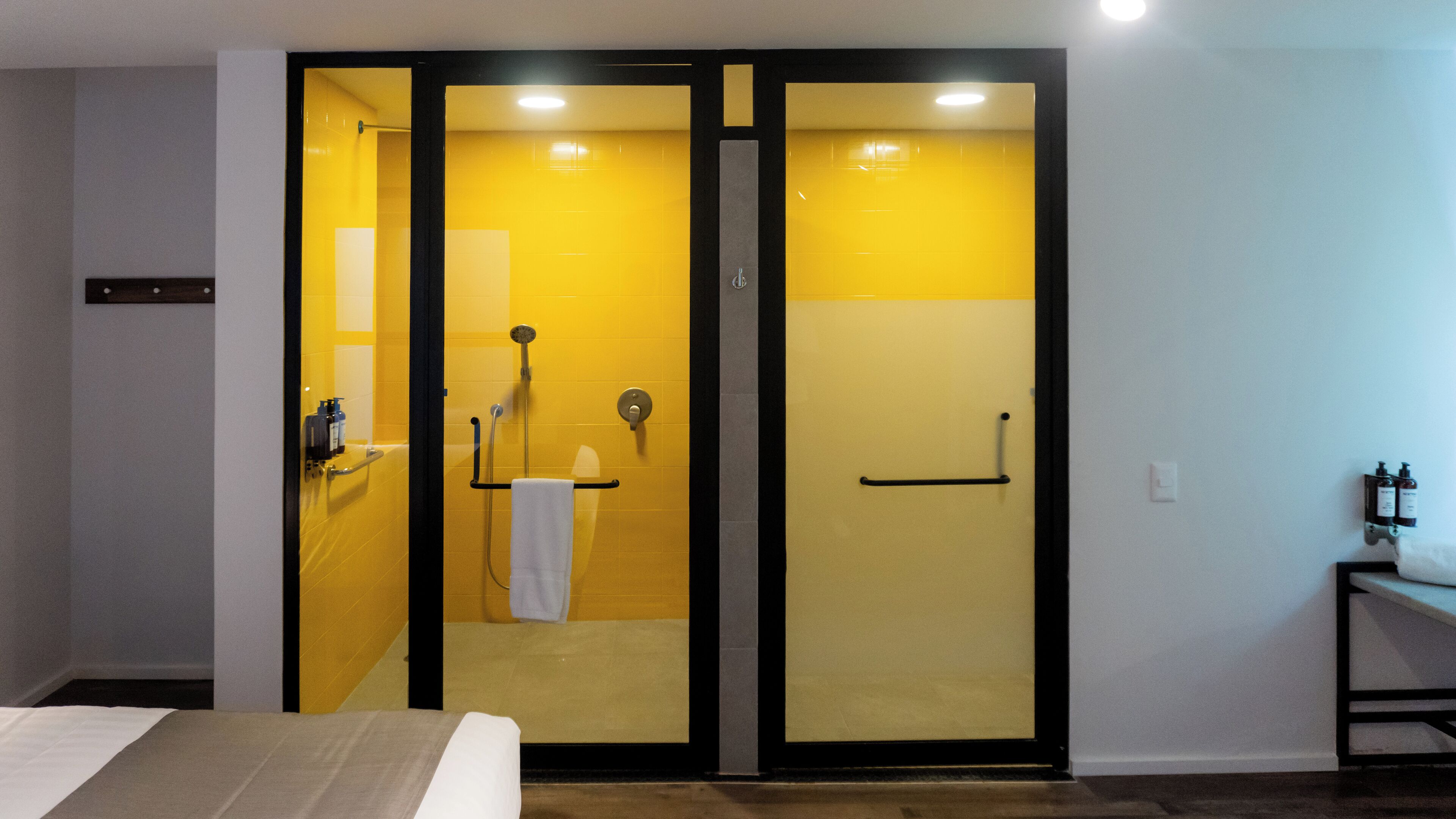 A hotel room with a bed, a bathroom with yellow walls, a shower, and a towel rack.
