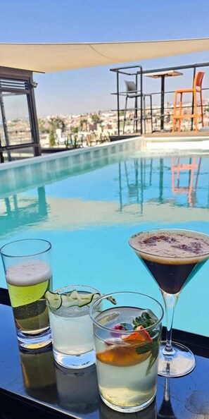 A poolside bar with a variety of drinks, a clear pool, and a view of the cityscape. - ALT Urbana (León)