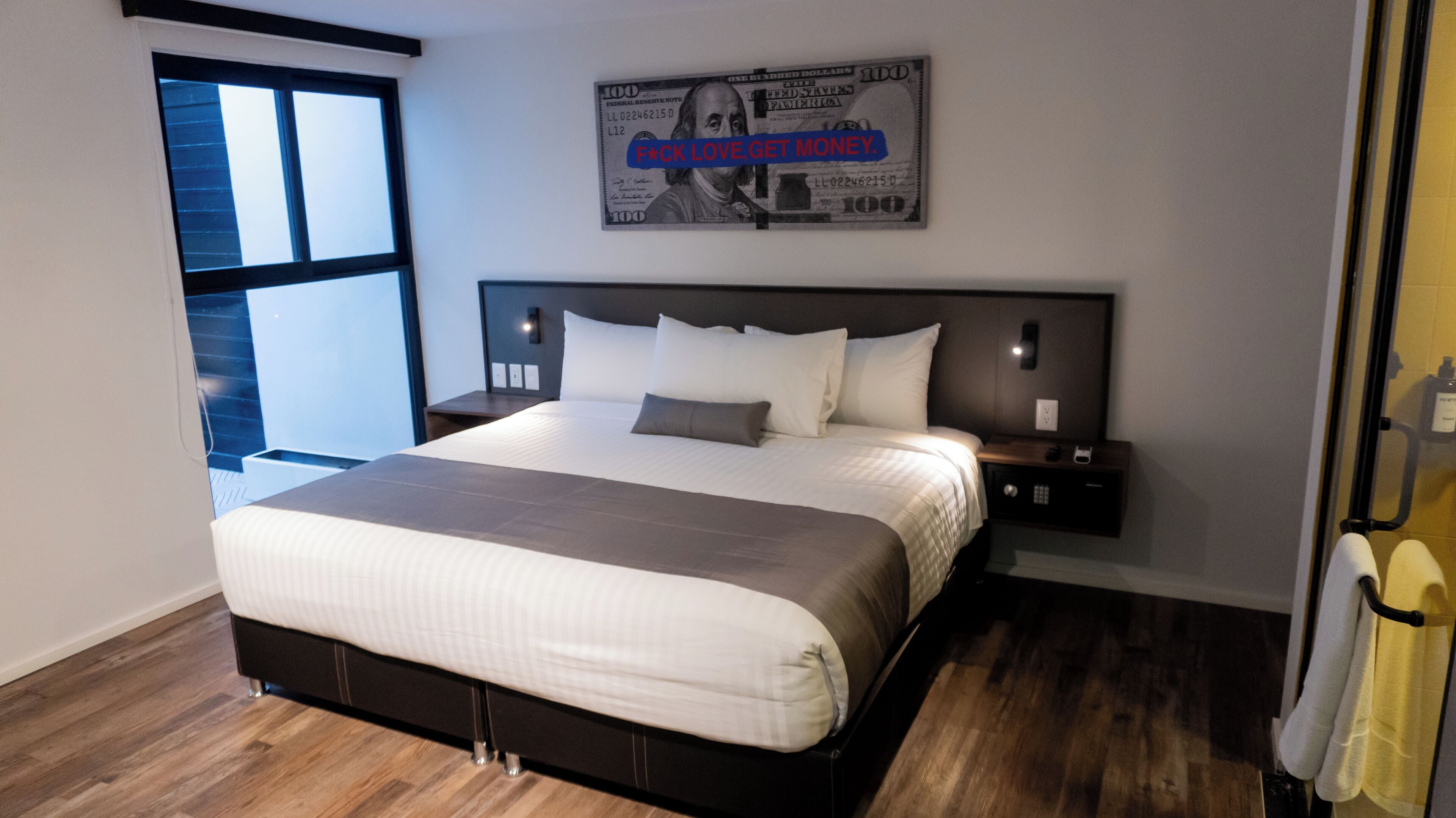 A modern hotel room with a large bed, a nightstand with a phone, and a window with blinds.