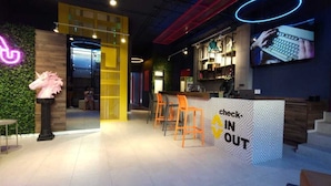A modern reception area with a neon sign, a check-in counter, and orange chairs. - ALT Urbana (León)