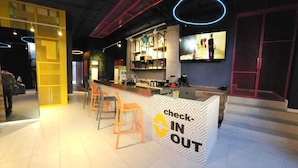 A modern bar area with a check-in/out counter, bar stools, and a television screen. - ALT Urbana (León)