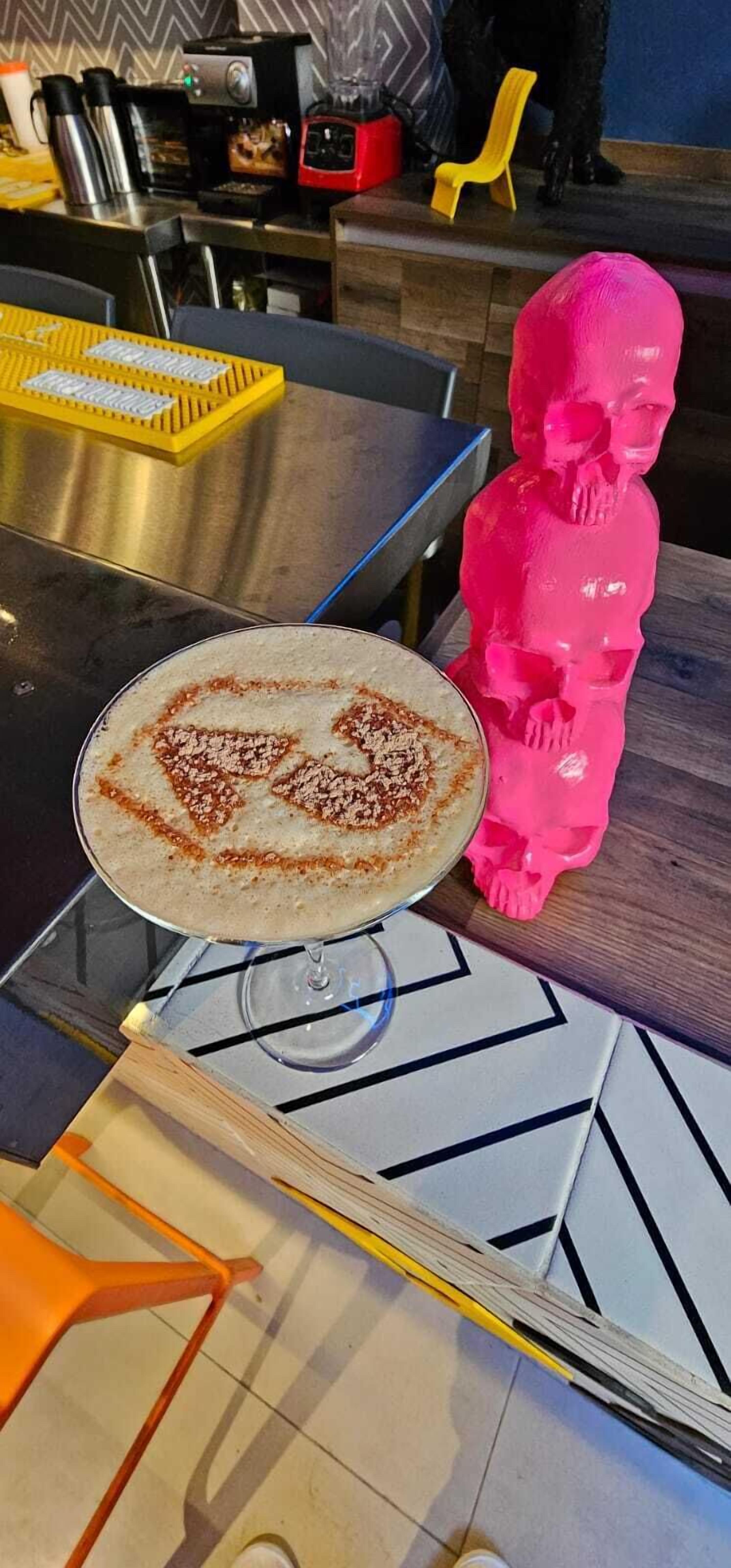 Una mesa con una bebida en un vaso, una figurita rosa y varios electrodomésticos de cocina.