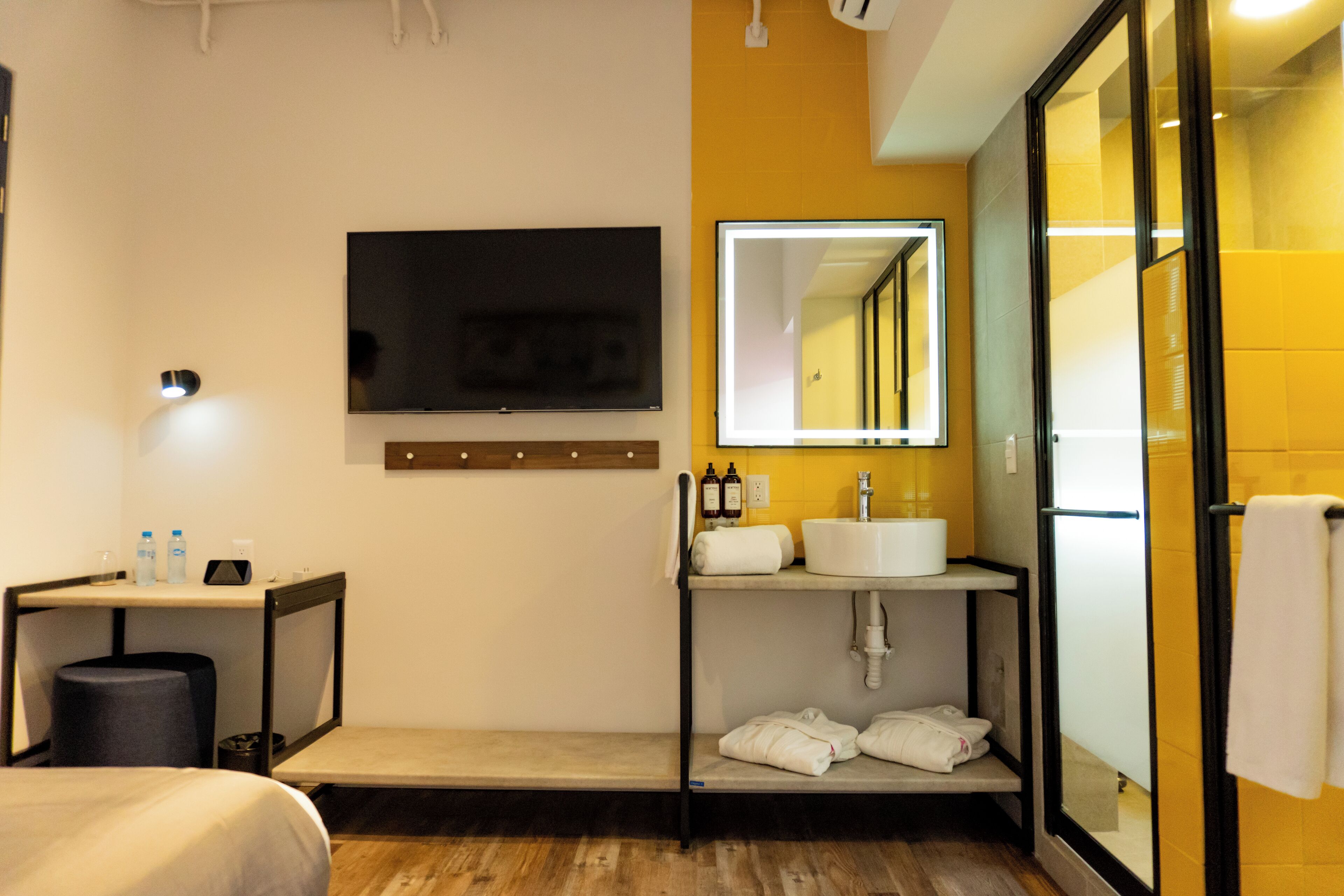 A modern hotel bathroom with a flat-screen TV, a large mirror, a sink, and a shower area.
