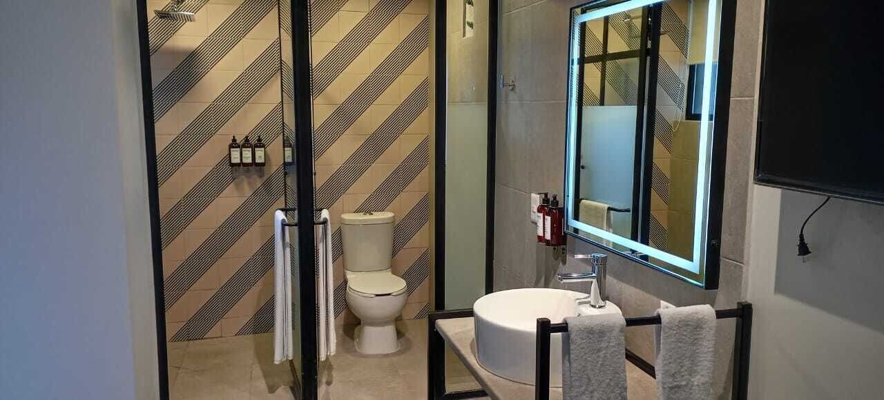 Um banheiro moderno com parede de azulejos listrados, vaso sanitário, pia com espelho e porta-toalhas.