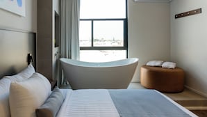 A modern hotel room with a large bed, a bathtub, and a view of the city. - ALT Urbana (León)